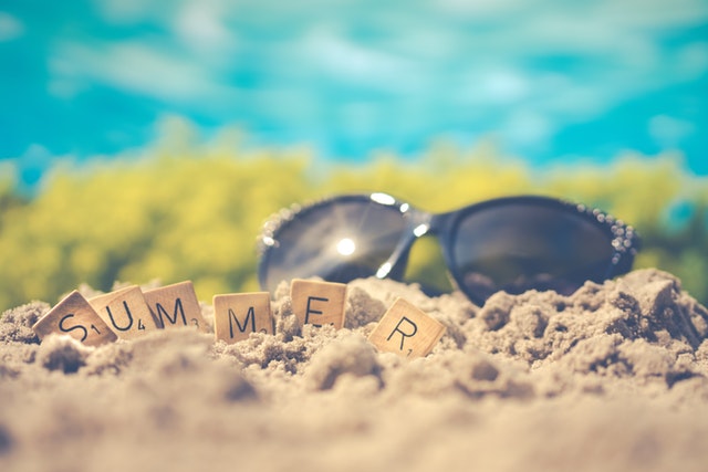 Slnečné okuliare a nápis „summer“ vyskladaný z drevených kociek položené v piesku.jpg